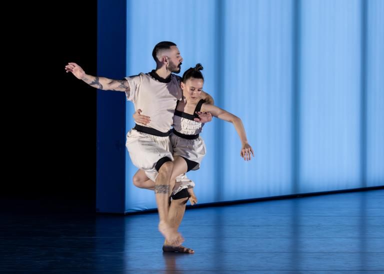 Dansarna Simone Frederick Scacchetti och Hanna Nussbaumer står tillsammans med ihopflätade ben och balanserar klädda i vita kläder med svarta detaljer i Skånes Dansteaters dansföreställning Out of the Blue. 