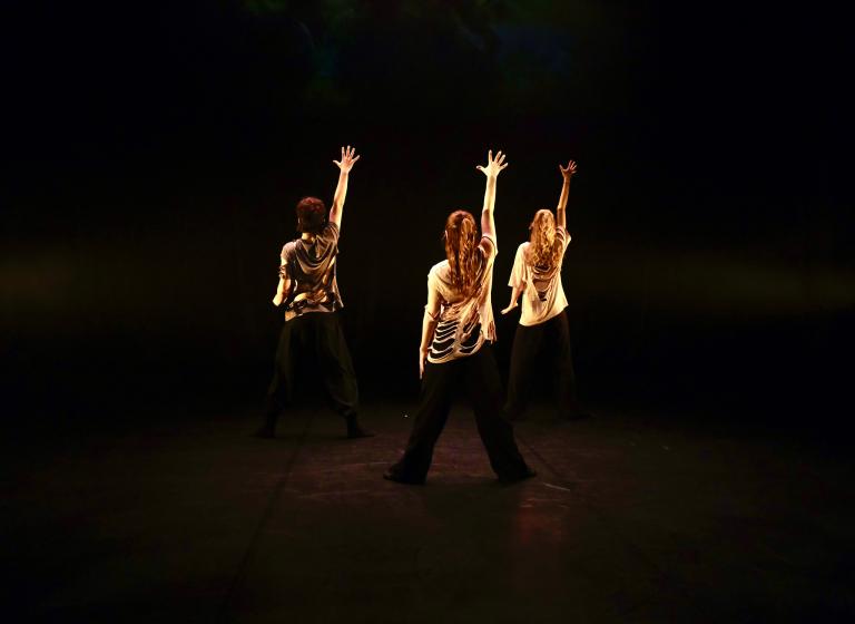 Tre danselever från Malmö Kulturskola står med ryggen mot dig med en arm uppsträckt.