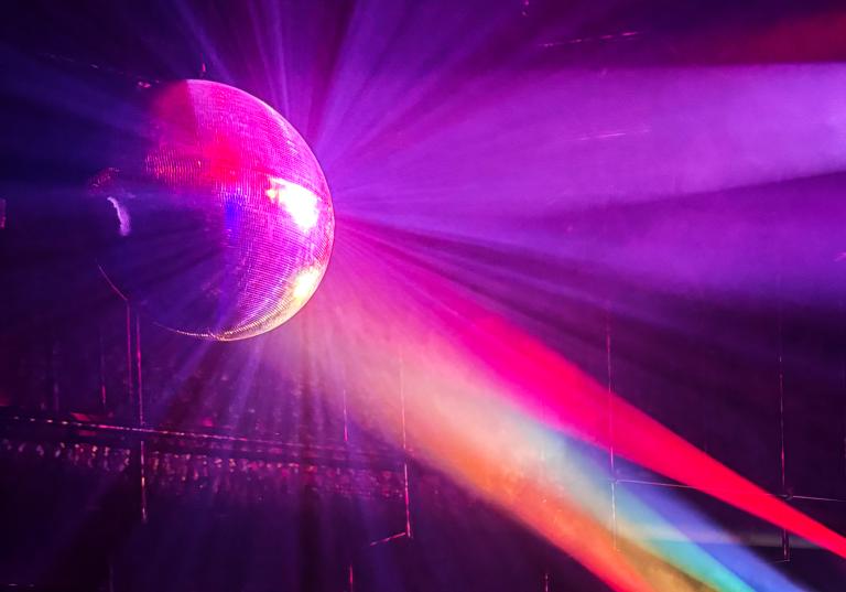 Strålkastarljus i rött, blått, grönt och gult lyser på en discoboll.
