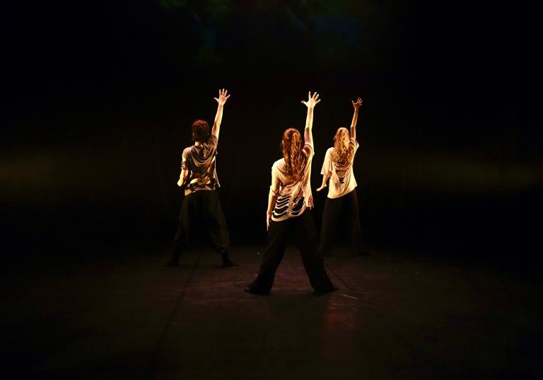 Tre danselever från Malmö Kulturskola står med ryggen mot dig med en arm uppsträckt.
